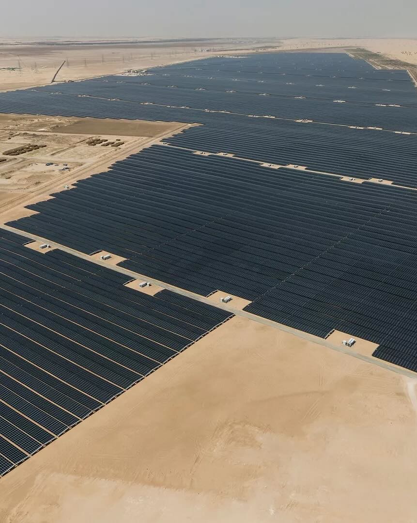 A large-scale solar power plant with rows of photovoltaic panels in a desert environment shown from the sky.
